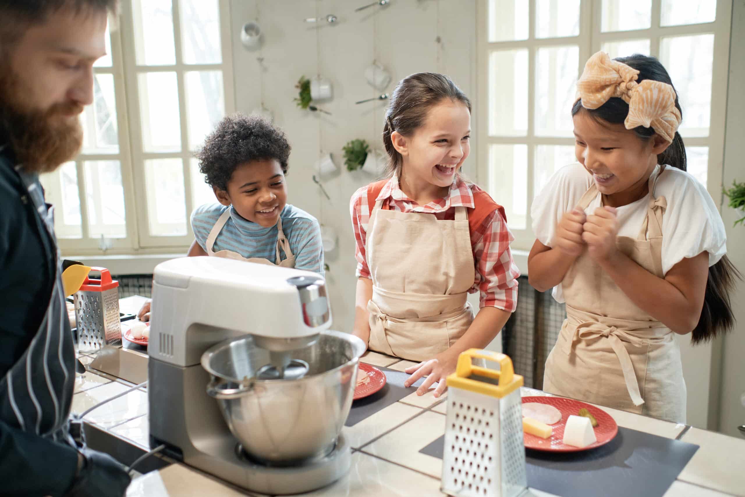 Group of happy children laughing during cooking lesson with cook in the kitchen